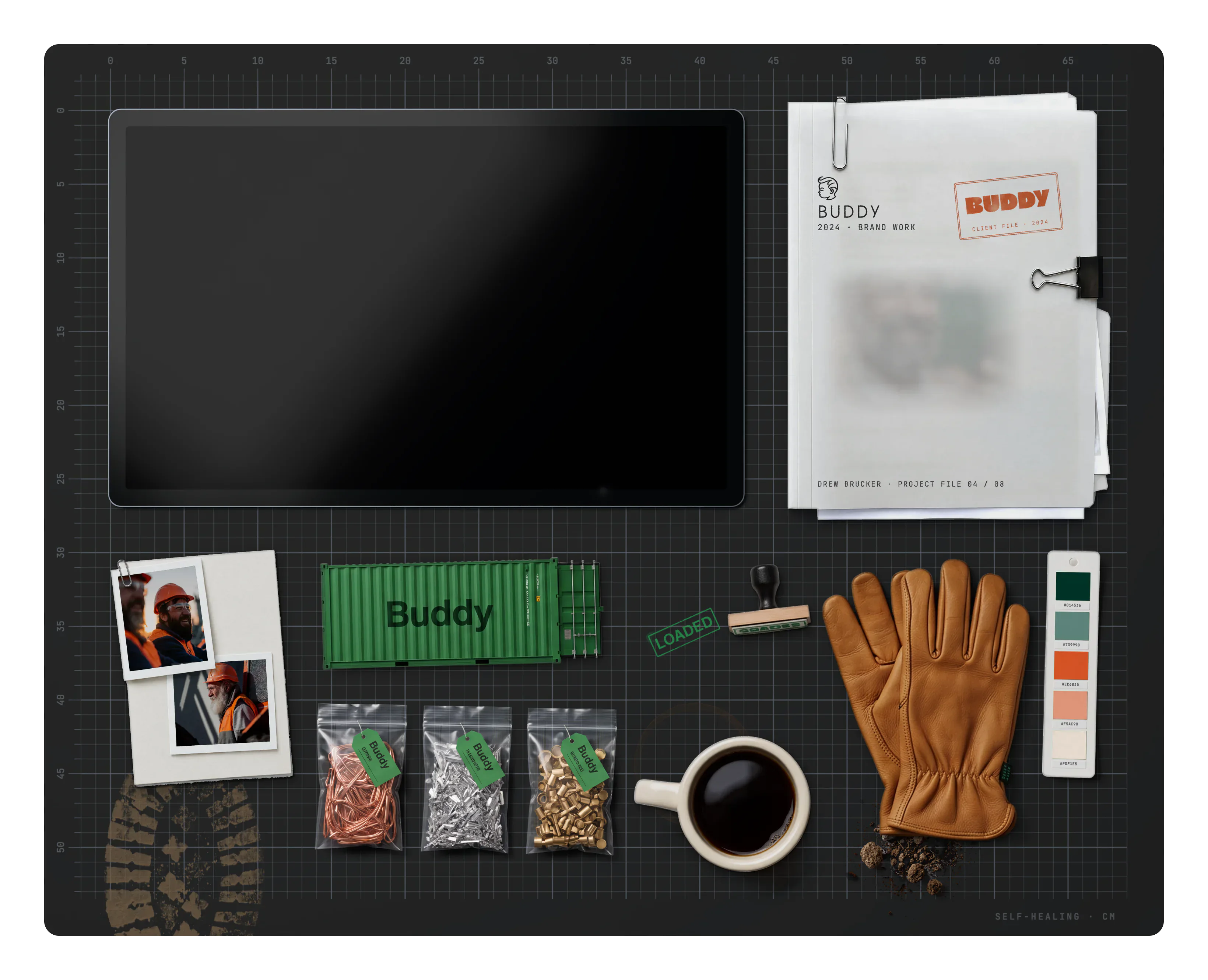 Buddy on the desk: the project file, a muddy boot print, clipped prints, a Buddy shipping container model, bagged scrap metal samples, a coffee ring, a mug of coffee, a LOADED stamp mark, a LOADED rubber stamp, a little dirt, leather work gloves and the brand swatch