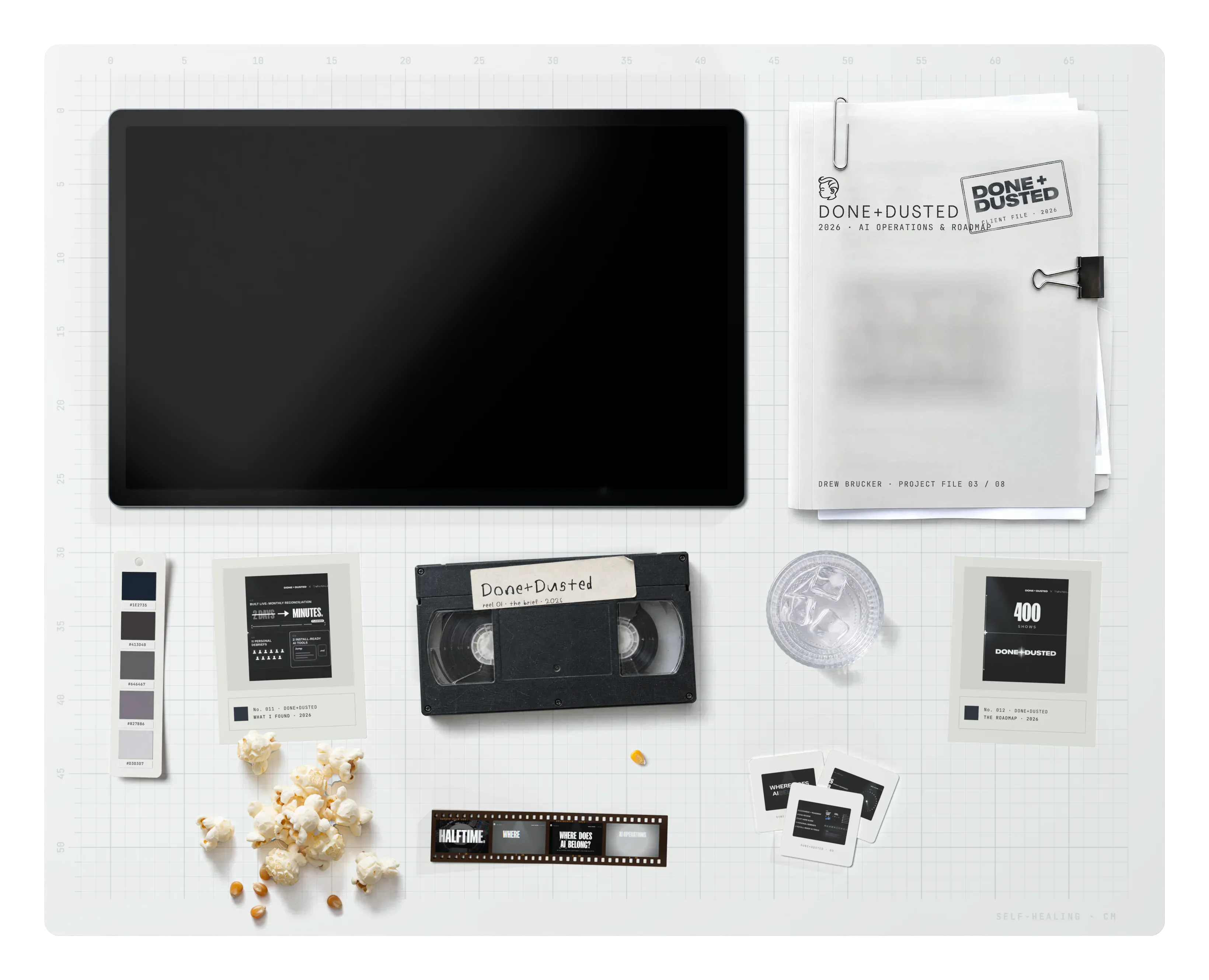 Done+Dusted on the desk: the project file, the brand swatch, archive cards, a VHS tape, a film strip, a glass of water, slides and spilled popcorn