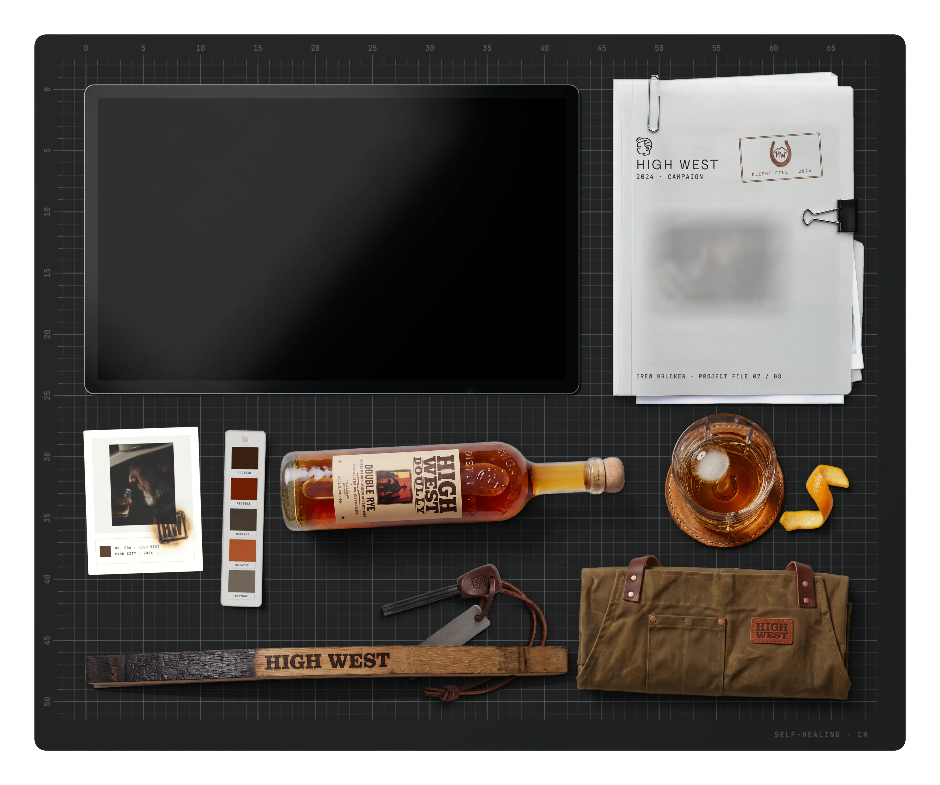 High West on the desk: the project file, archive cards, the brand swatch, a bottle of High West Double Rye, a whiskey on the rocks, an orange peel twist, a ferro rod fire starter, a charred barrel stave branded HIGH WEST and a waxed canvas apron roll